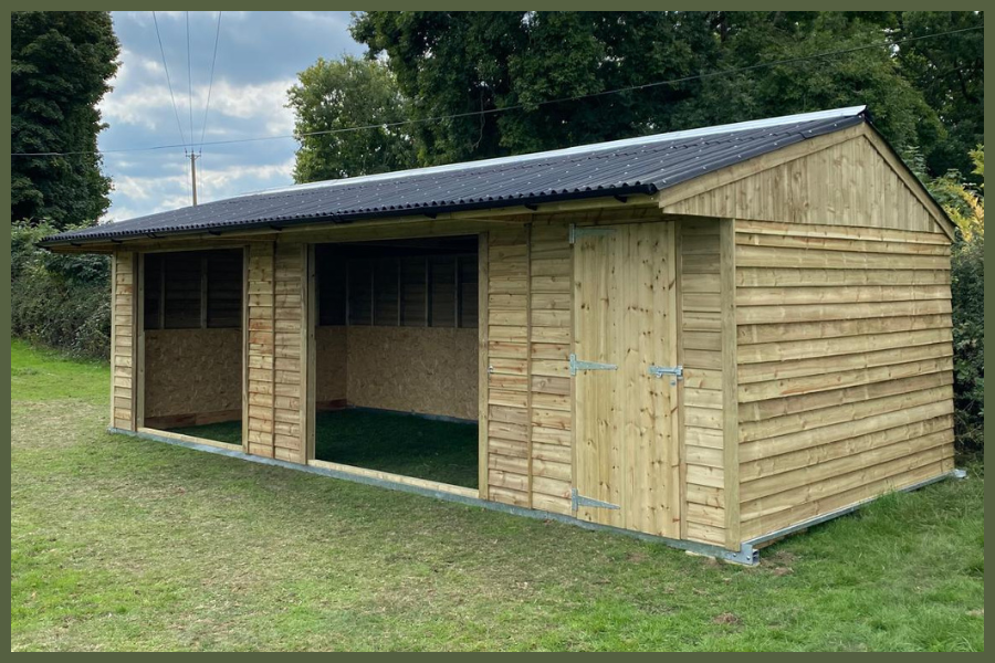 Timber field shelter with 2 open-front doorways, and a 6ft tack room pressure-treated cladding and onduline roofing, built by Longcross Stables.
